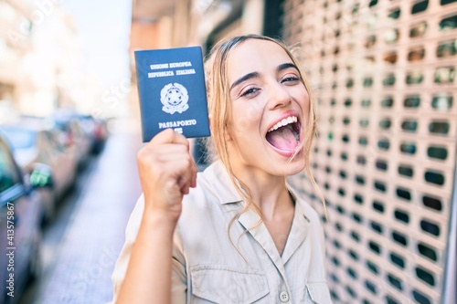 Young beautiful blonde caucasian woman smiling happy outdoors on a sunny day showing Italy passport photo