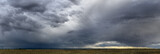 Dramatic blue-gray storm clouds over a very wide panoramic prairie landscape with a gravel road extending off into the distance. 