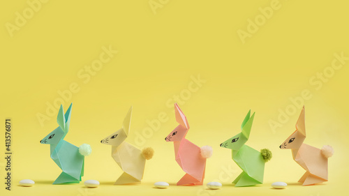 Paper Easter bunnies-origami made of colored paper on a delicate yellow background. The concept of the celebration of Easter  greeting card  crafts with your own hands.