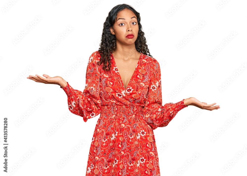 Young african american girl wearing summer dress clueless and confused expression with arms and hands raised. doubt concept. Young african american girl wearing summer dress clueless and confused expression with arms and hands raised. doubt concept.