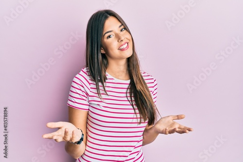 Young brunette woman wearing casual clothes over pink background smiling cheerful with open arms as friendly welcome, positive and confident greetings © Krakenimages.com