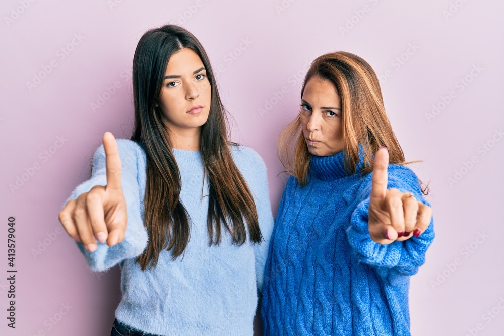 Hispanic family of mother and daughter wearing wool winter sweater pointing with finger up and angry expression, showing no gesture Hispanic family of mother and daughter wearing wool winter sweater pointing with finger up and angry expression, showing no gesture