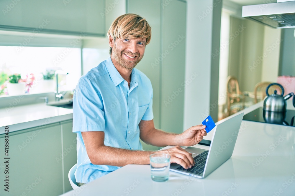 Young irish man using credit card and laptop to buy sitting on the table at home. Young irish man using credit card and laptop to buy sitting on the table at home.