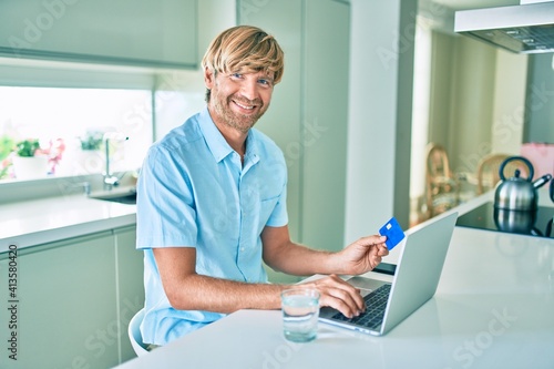 Young irish man using credit card and laptop to buy sitting on the table at home.