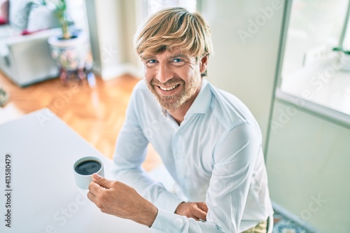Young irish man smiling happy drinking cup of coffee sitting on the table at home.