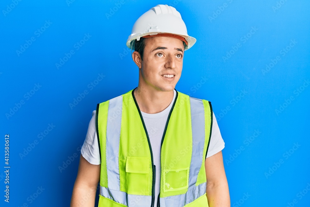 Handsome young man wearing safety helmet and reflective jacket looking away to side with smile on face, natural expression. laughing confident. Handsome young man wearing safety helmet and reflective jacket looking away to side with smile on face, natural expression. laughing confident.