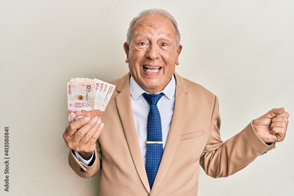 Senior caucasian man holding 10 colombian pesos banknotes screaming proud, celebrating victory and success very excited with raised arm Senior caucasian man holding 10 colombian pesos banknotes screaming proud, celebrating victory and success very excited with raised arm