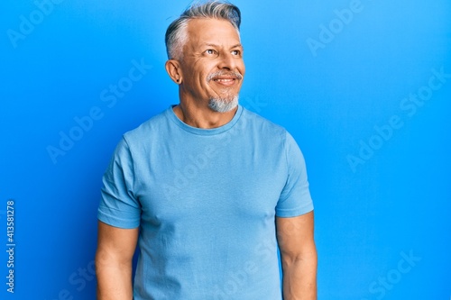 Middle age grey-haired man wearing casual clothes looking away to side with smile on face, natural expression. laughing confident.