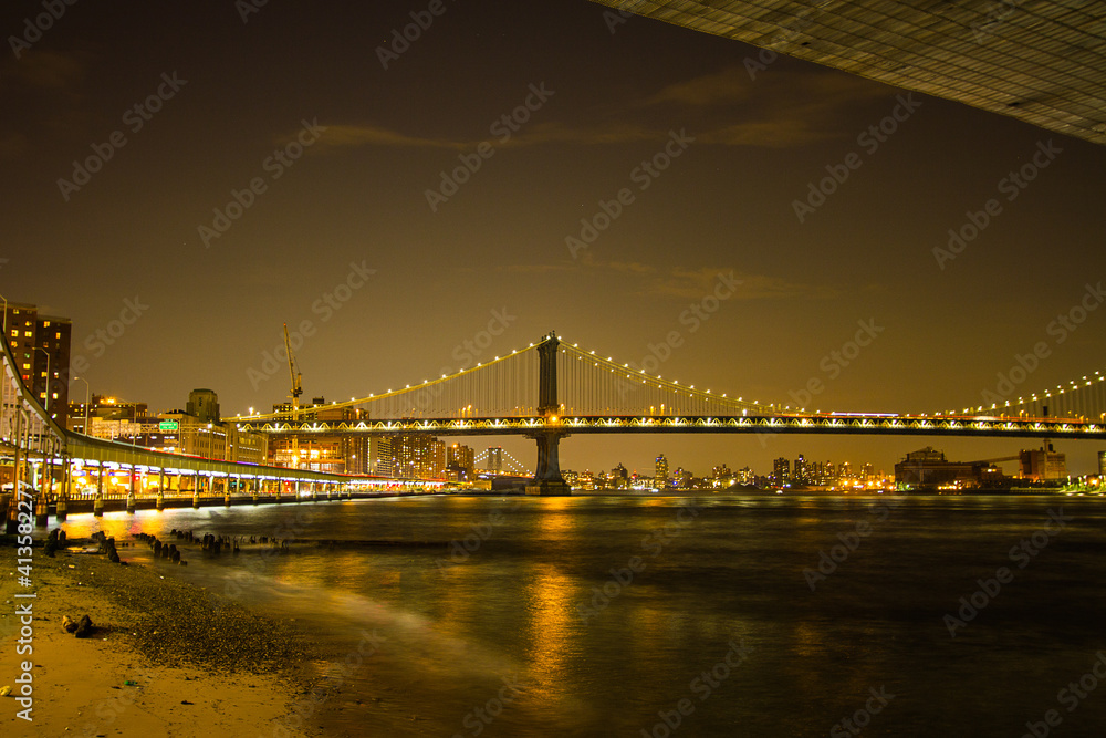 Manhattan Bridge seen from East River Greenway at night with the city light reflections on the river 