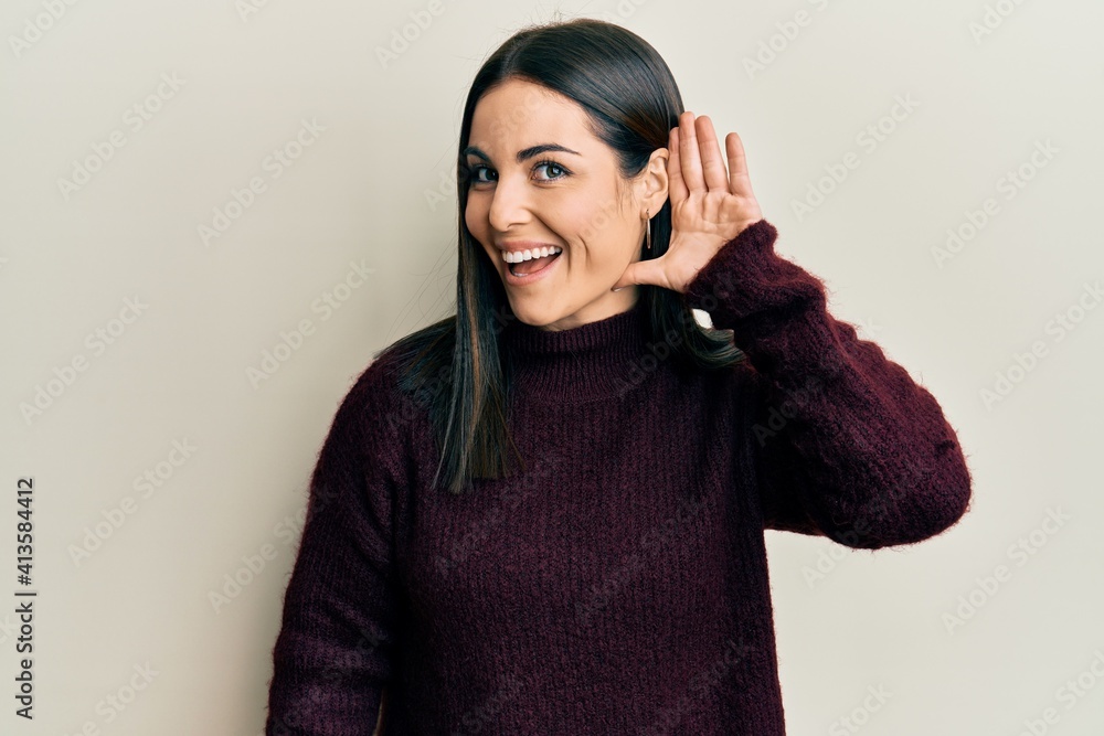 Young brunette woman wearing casual winter sweater smiling with hand over ear listening and hearing to rumor or gossip. deafness concept. Young brunette woman wearing casual winter sweater smiling with hand over ear listening and hearing to rumor or gossip. deafness concept.