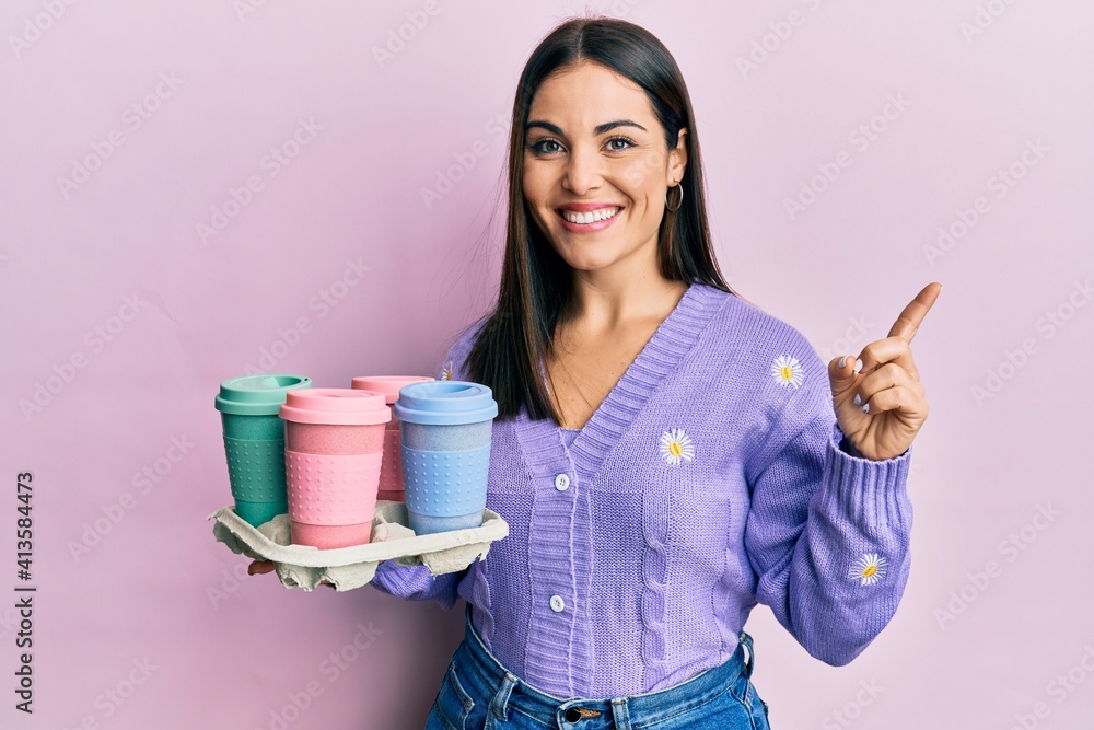 Young brunette woman holding tray with take away coffee smiling happy pointing with hand and finger to the side Young brunette woman holding tray with take away coffee smiling happy pointing with hand and finger to the side