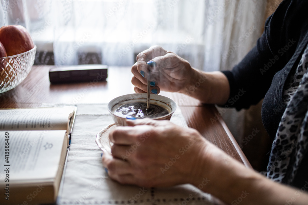 cup of coffee on the table, old woman's hands stir coffee