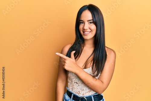 Young beautiful hispanic girl wearing casual clothes smiling cheerful pointing with hand and finger up to the side