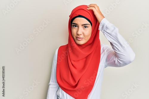 Young beautiful hispanic girl wearing traditional islamic hijab scarf confuse and wonder about question. uncertain with doubt, thinking with hand on head. pensive concept. © Krakenimages.com