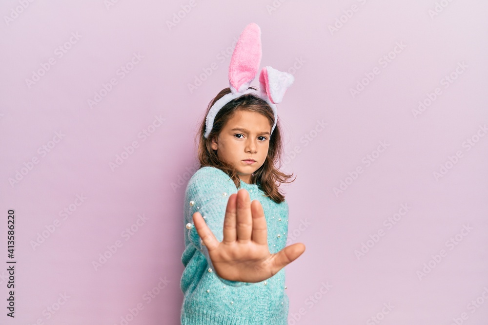 Little beautiful girl wearing cute easter bunny ears doing stop sing with palm of the hand. warning expression with negative and serious gesture on the face. Little beautiful girl wearing cute easter bunny ears doing stop sing with palm of the hand. warning expression with negative and serious gesture on the face.