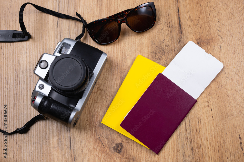 The concept of new normal conditions of tourism. On the wooden table are photo camera, sunglasses, passport, international certificate of vaccination, flying ticket. Top view. Ready for safe tour The concept of new normal conditions of tourism. On the wooden table are photo camera, sunglasses, passport, international certificate of vaccination, flying ticket. Top view. Ready for safe tour