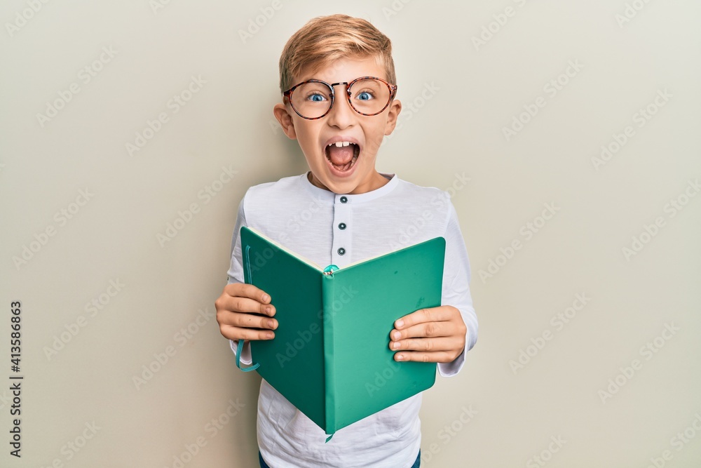 Little caucasian boy kid reading a book wearing glasses celebrating crazy and amazed for success with open eyes screaming excited. Little caucasian boy kid reading a book wearing glasses celebrating crazy and amazed for success with open eyes screaming excited.