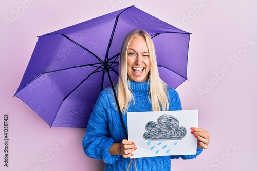 Young blonde girl holding umbrella rain draw winking looking at the camera with sexy expression, cheerful and happy face. © Krakenimages.com