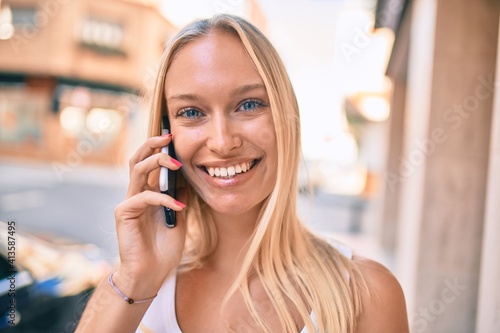 Young blonde girl smiling happy talking on the smartphone at the city.