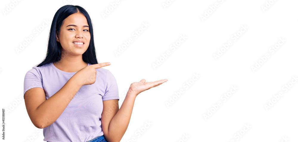 Young beautiful asian girl wearing casual clothes amazed and smiling to the camera while presenting with hand and pointing with finger. Young beautiful asian girl wearing casual clothes amazed and smiling to the camera while presenting with hand and pointing with finger.