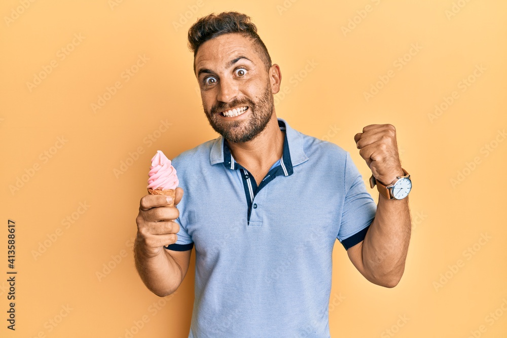 Handsome man with beard eating ice cream cone screaming proud, celebrating victory and success very excited with raised arm Handsome man with beard eating ice cream cone screaming proud, celebrating victory and success very excited with raised arm