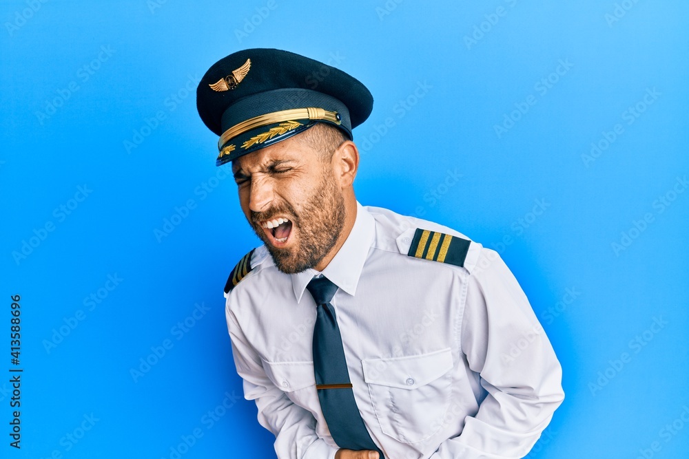 Handsome man with beard wearing airplane pilot uniform with hand on stomach because nausea, painful disease feeling unwell. ache concept. Handsome man with beard wearing airplane pilot uniform with hand on stomach because nausea, painful disease feeling unwell. ache concept.