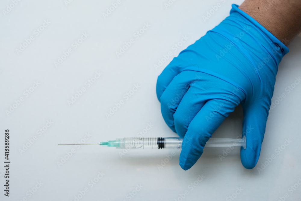 Hand wearing a blue medical glove using a injection on a white surface Hand wearing a blue medical glove using a injection on a white surface