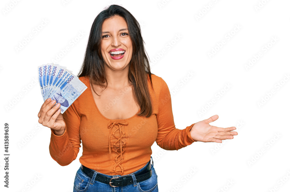 Beautiful hispanic woman holding 1000 south korean won banknotes celebrating victory with happy smile and winner expression with raised hands Beautiful hispanic woman holding 1000 south korean won banknotes celebrating victory with happy smile and winner expression with raised hands