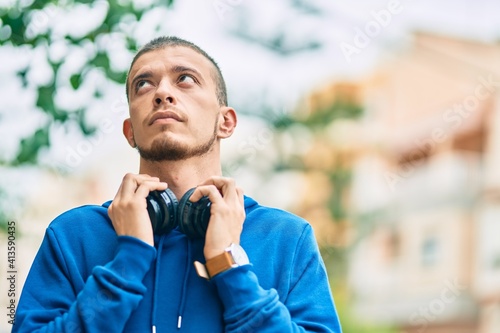 Young hispanic man with serious expression using headphones at the city
