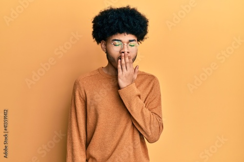 Young african american man with afro hair wearing casual winter sweater bored yawning tired covering mouth with hand. restless and sleepiness. © Krakenimages.com