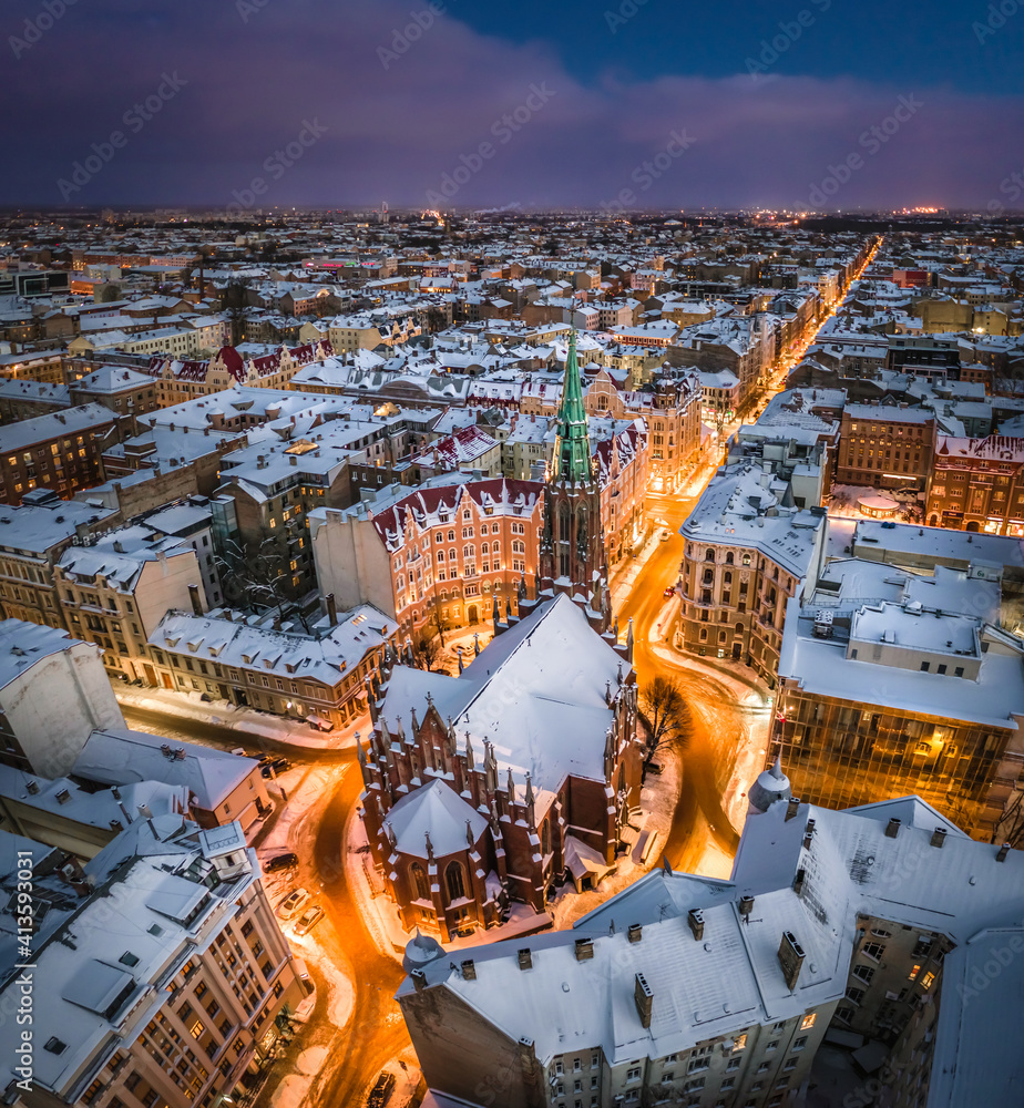 Riga city panorama in winter time. Street lights glowing in blue hour. Snowy rooftops. Iconic buildings and architecture. Drone footage.