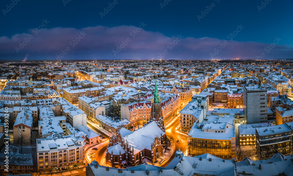 Obraz premium Riga city panorama in winter time. Street lights glowing in blue hour. Snowy rooftops. Iconic buildings and architecture. Drone footage.