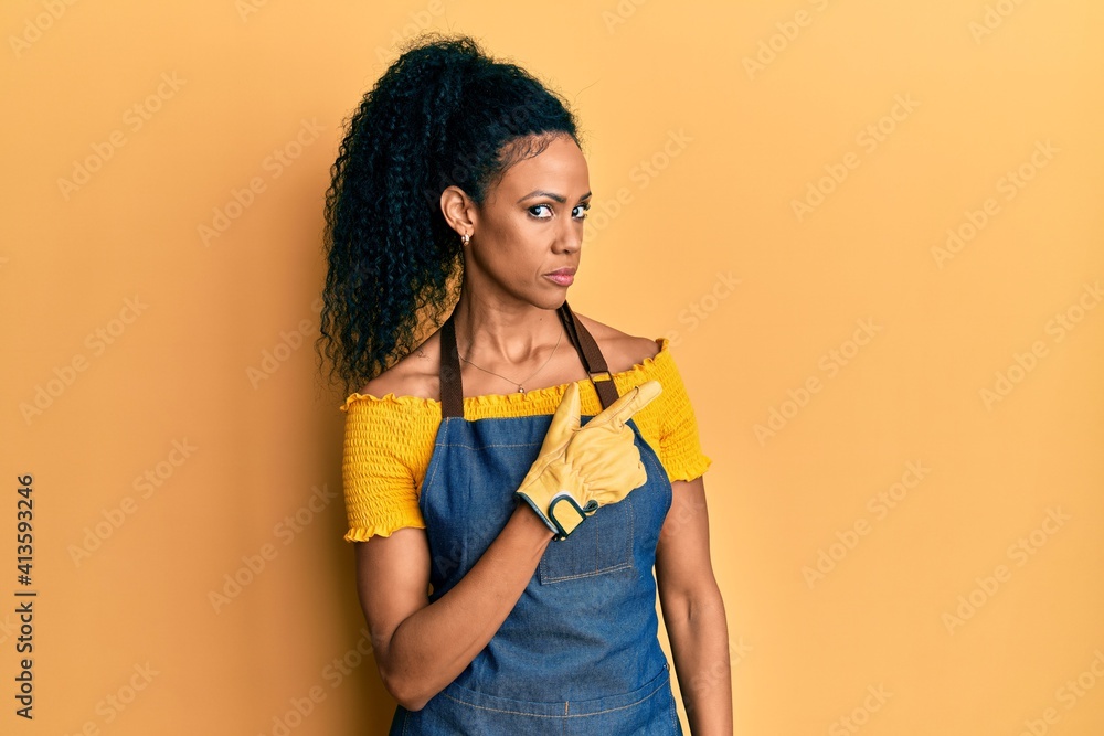 Middle age african american woman wearing professional apron pointing with hand finger to the side showing advertisement, serious and calm face Middle age african american woman wearing professional apron pointing with hand finger to the side showing advertisement, serious and calm face