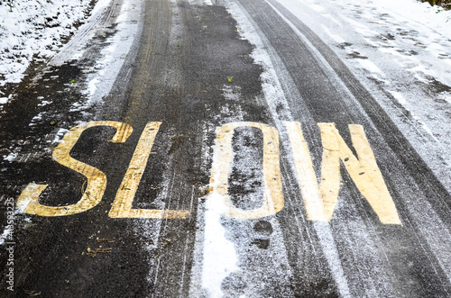 Slow sign on icy and snowy road in winter that can illustrate black ice and adverse weather conditions