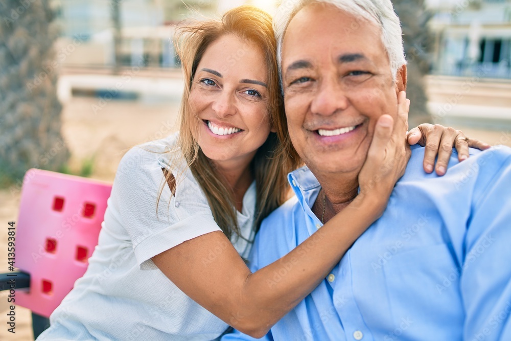 Middle age hispanic couple smiling happy and hugging sitting on bench at the beach. Middle age hispanic couple smiling happy and hugging sitting on bench at the beach.