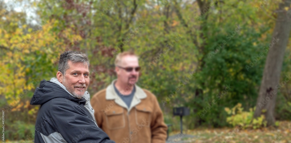 A middle-aged gay couple goes for a walk in the park with their dog in the autumn. A middle-aged gay couple goes for a walk in the park with their dog in the autumn.