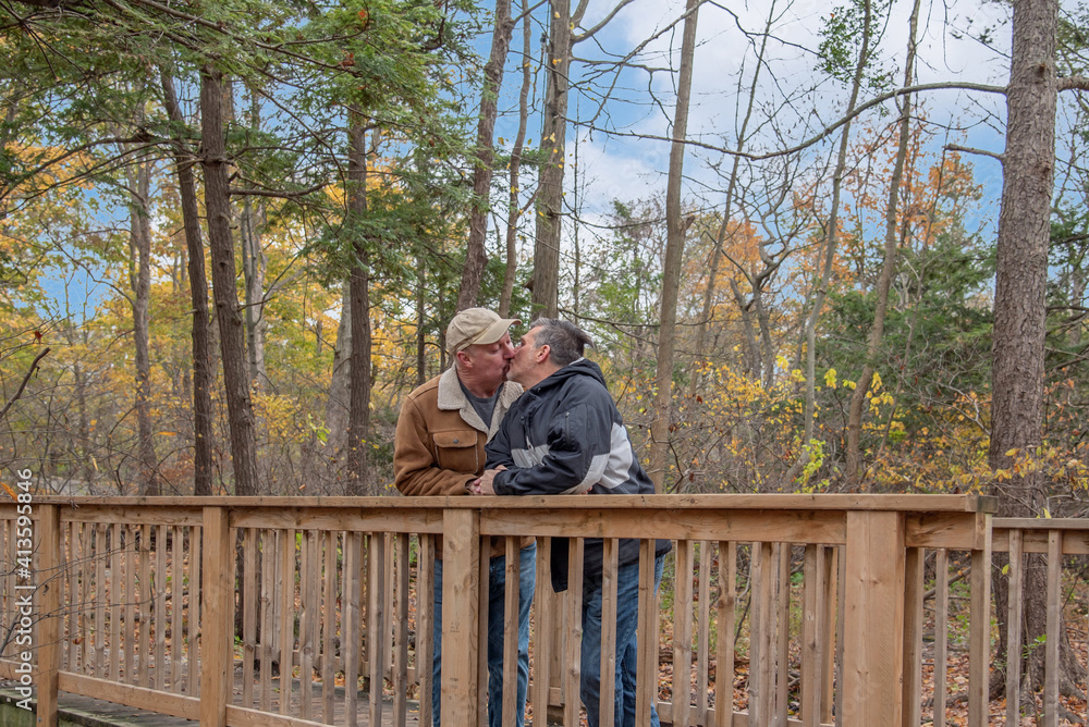 Fototapeta premium A middle-aged gay couple goes for a walk in the park with their dog in the autumn.