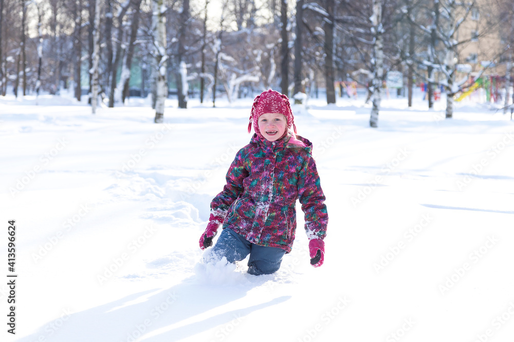 Winter activities outdoors. Positive little girl wearing a warm clothes walking through the snowdrifts in snowy park on cheerful winter day