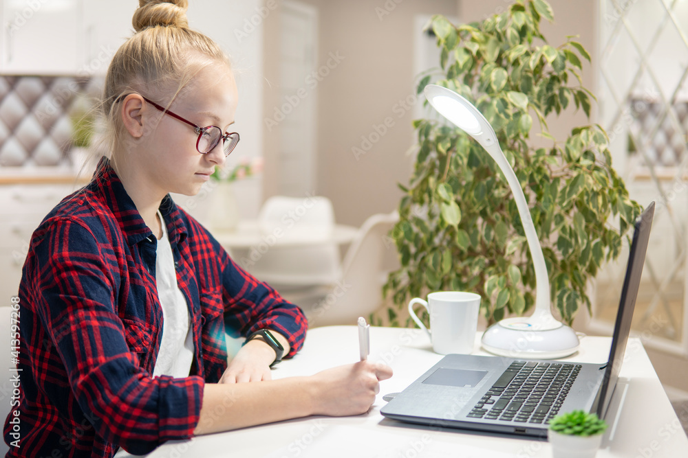 Blonde girl with glasses work on a laptop at home. Home-school concept