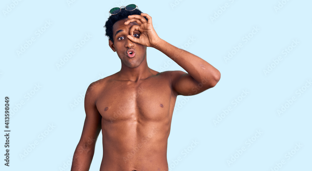 Fototapeta premium African handsome man wearing swimsuit and sunglasses doing ok gesture shocked with surprised face, eye looking through fingers. unbelieving expression.