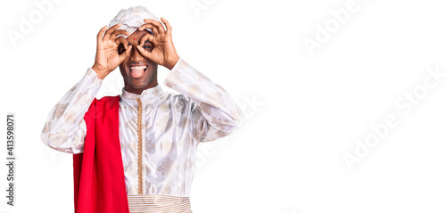 African handsome man wearing tradition sherwani saree clothes doing ok gesture like binoculars sticking tongue out, eyes looking through fingers. crazy expression.