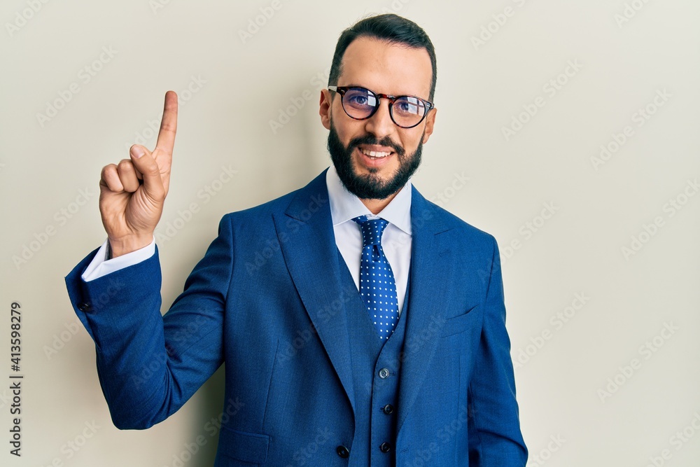 Young man with beard wearing business suit and tie showing and pointing up with finger number one while smiling confident and happy. Young man with beard wearing business suit and tie showing and pointing up with finger number one while smiling confident and happy.