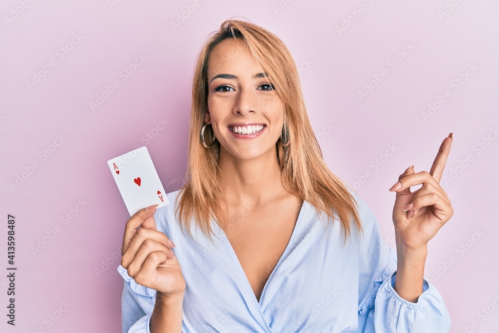 Beautiful blonde woman holding ace poker card smiling happy pointing with hand and finger to the side Beautiful blonde woman holding ace poker card smiling happy pointing with hand and finger to the side