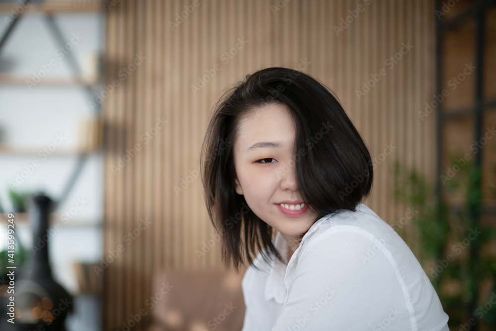 Portrait of a beautiful Asian young woman in a white fashionable shirt at home in a dark loft design interior. Portrait of a beautiful Asian young woman in a white fashionable shirt at home in a dark loft design interior.