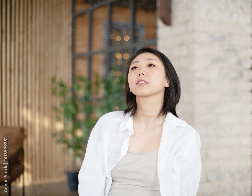 Portrait of a beautiful Asian young woman in a white fashionable shirt at home in a dark loft design interior.