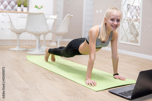 young attractive girl is engaged in fitness at home and looks at the laptop. quarantine fitness concept