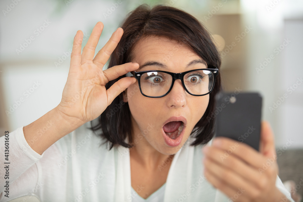 woman wearing eyeglasses looking with shock at smartphone