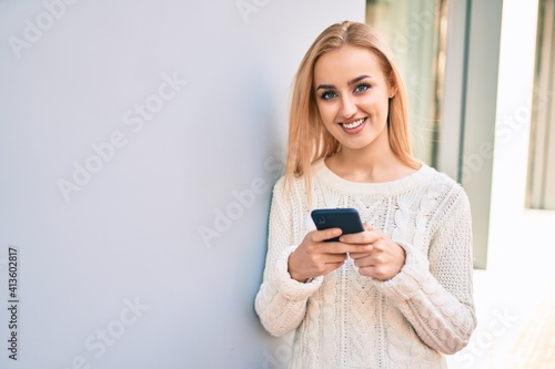 Young blonde girl smiling happy using smartphone at the city.