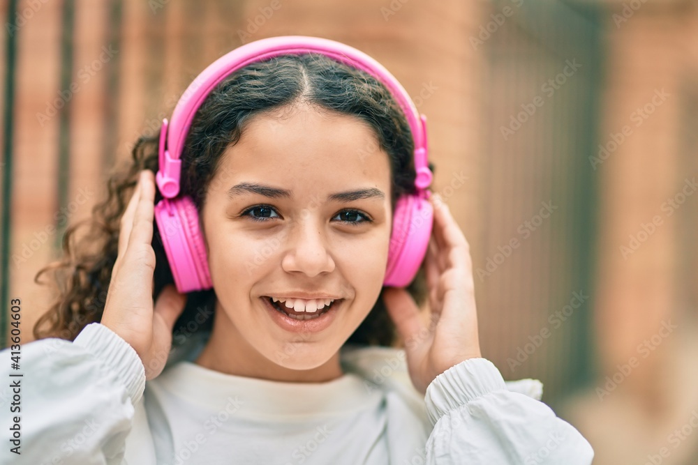 Hispanic child girl smiling happy using headphones at the city. Hispanic child girl smiling happy using headphones at the city.