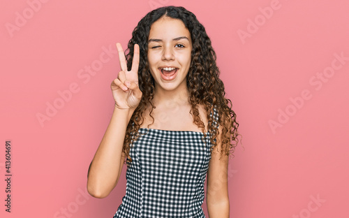 Teenager hispanic girl wearing casual clothes smiling with happy face winking at the camera doing victory sign. number two.